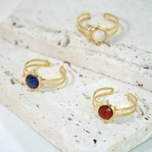 Detail view of gold stainless steel rings with colorful inlaid stones on a stone surface