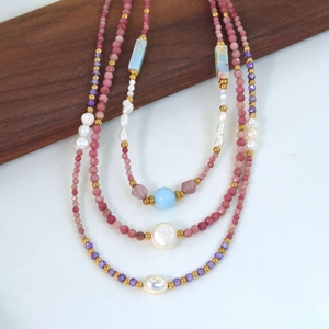 Collana fatta a mano con ametista, perle e pietre rosa su superficie in legno e tessuto