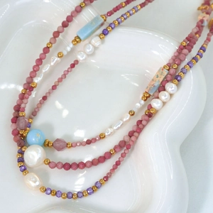 Macro di una collana con perle, ametista e pietre naturali su un vassoio bianco lucido