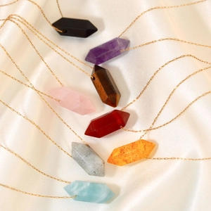 Minimalist bullet-shaped crystal pendant necklaces on gold chains over silk background