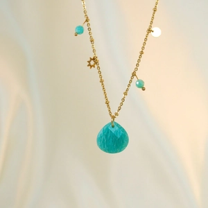Detail der Goldkette mit facettiertem blauem Stein und Sternanhängern auf Stoff