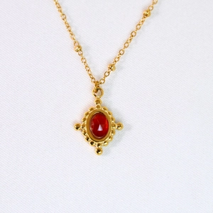 Détail d'un collier vintage doré avec pendentif en agate rouge et chaîne perlée
