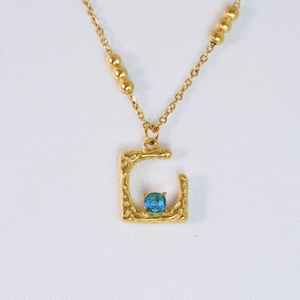 Detalle de primer plano del colgante letra G en oro de 14k con circón azul y textura