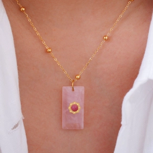 Close-up of a rectangle pink natural stone pendant with gold octagon detail on a chain