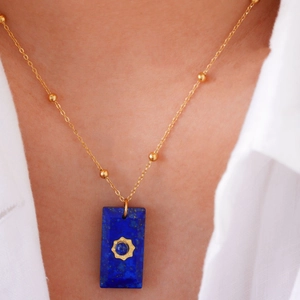 Detail of bohemian necklace with blue stone pendant and golden sunburst motif
