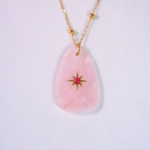 Detail of pink rose quartz pendant with gold starburst inlay on a gold beaded chain