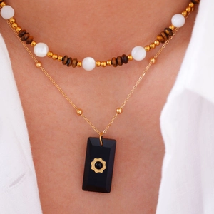 Detail of layered gold necklace with beaded strand and black rectangular flower pendant