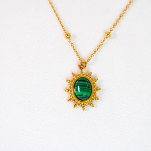 Vista macro di una collana in oro con ciondolo a sole e pietra di malachite verde