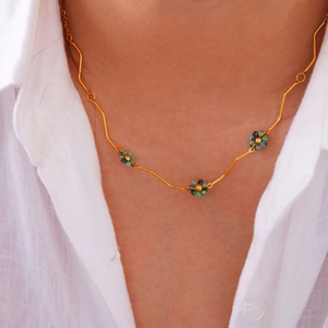 Golden stainless steel wavy chain necklace with turquoise bead flower charms on linen shirt