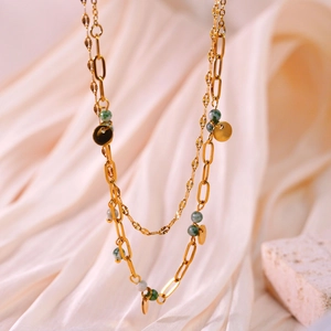 Detail of layered gold necklace with paperclip chain, green stones and round pendants