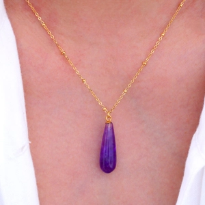 Nahaufnahme einer Goldkette mit tropfenförmigem lila Steinanhänger an einem Modell