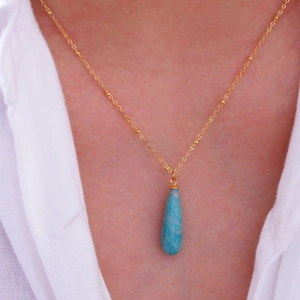 Nahaufnahme des blauen Tropfen-Anhängers mit goldener Kugelkette am Frauenhals