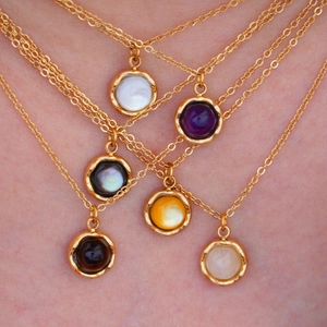 Detail of layered gold necklaces featuring round natural stone pendants with hammered texture