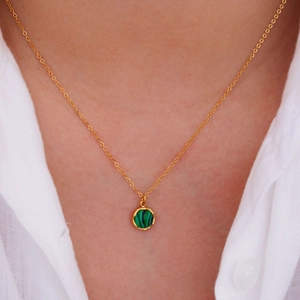 Golden necklace with round green malachite pendant worn on a model with white shirt