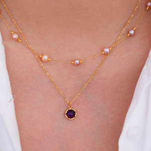 Detail of layered gold necklace with pink pearls and a bezel-set purple gemstone pendant