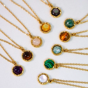 Collection of colorful faceted gemstone necklaces with gold wavy bezel settings on white fabric