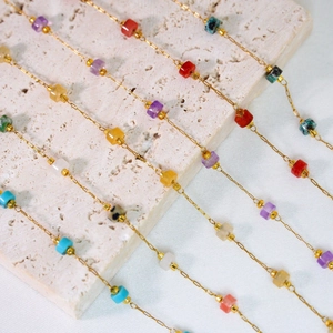 Collares de cadena dorada con piedras naturales cuadradas de colores sobre fondo de piedra