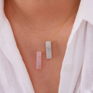 Dettaglio di collane d'oro a strati con pendenti in pietra rosa e marmo su camicia bianca