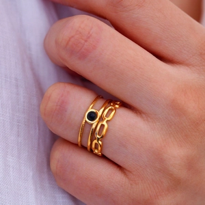 Detail of three-piece gold-toned ring set with black circular inlay and link chain design