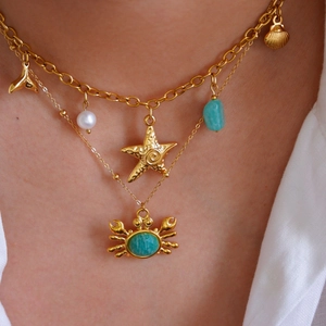 Close-up of a layered gold necklace featuring a crab pendant and turquoise stones