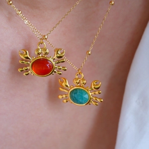 Close-up of golden crab necklaces with red and turquoise gemstones on a model wearing white shirt
