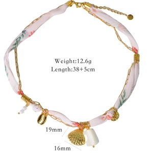 Détail de breloques coquillage et perles sur un collier ruban fleuri rose et or