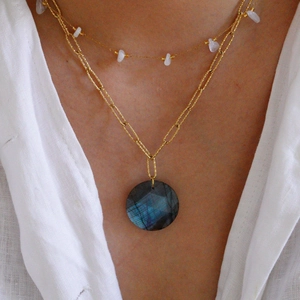 Detalle de collar dorado de capas con colgante de labradorita azul y piedras blancas