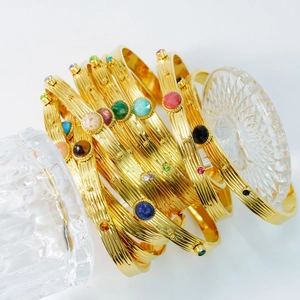 Pulseras apilables de acero dorado con gemas coloridas en un soporte de cristal