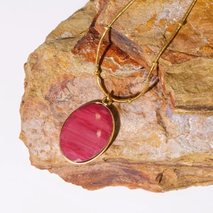 Detailopname van de ovale roze natuurstenen hanger met gouden rand op een ruwe rots