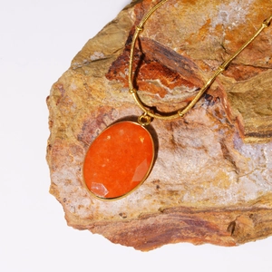 Macro-opname van een ovale gefacetteerde oranje steenhanger aan een goudkleurige ketting