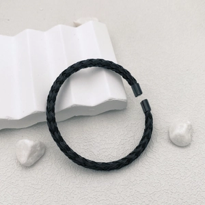 Macro detail of black braided titanium steel open bangle on minimalist stone background