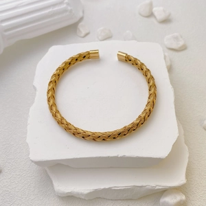 Detailed view of golden woven titanium steel open bangle on white textured stone background