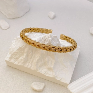 Minimalist gold braided woven open bangle bracelet on elegant white decorative stones