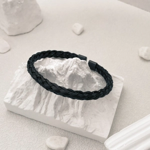 Close-up of black braided titanium steel bracelet on a minimalist white stone display
