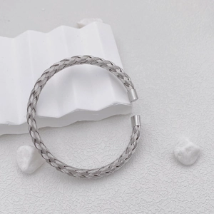 Polished silver woven titanium steel open bangle with braided texture on a white pedestal