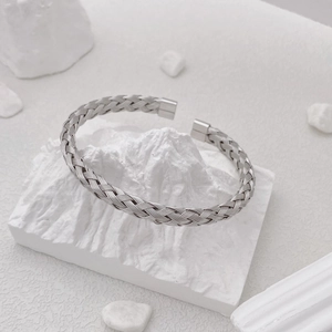 Detail of silver woven titanium steel cuff bracelet on a white minimalist stone base