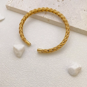 Detail of gold woven titanium steel bangle on travertine stone with white gravel