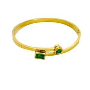 Bracciale dorato aperto con pietre verdi a taglio smeraldo e a forma di cuore su bianco