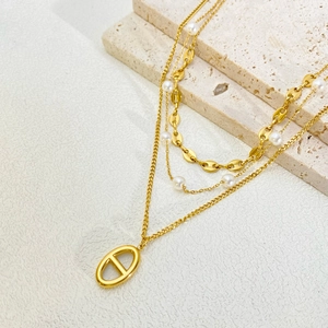 Detail of triple-layer gold necklace featuring pearls and oval link pendant on stone