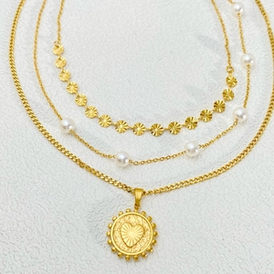 Detail of layered gold-tone necklace with pearl accents and heart coin pendant charms