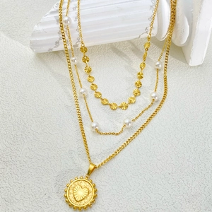 Detail of layered gold necklace with pearl accents and heart-textured coin pendant
