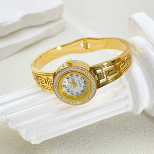 Close-up of gold quartz watch bangle featuring Greek meander pattern and crystal bezel
