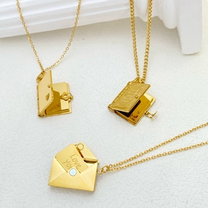 Macro detail of 18k gold plated envelope and book locket pendants with Love You engraving