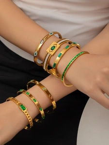 Dettaglio di bracciali in titanio placcati oro 18k con zirconi verdi e design evil eye