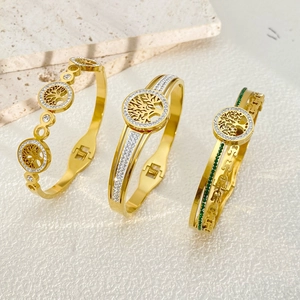 Three gold Tree of Life bracelets with crystals and green gems on a stone background