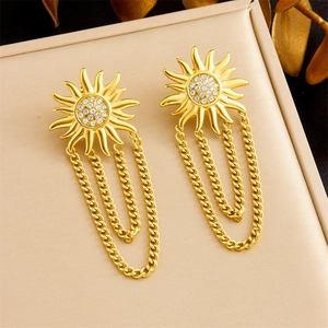 Close-up of golden sun-shaped tassel earrings with pavé zircons on a leather tray