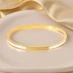 Close-up of golden stainless steel bangle with white shell inlay and geometric motif