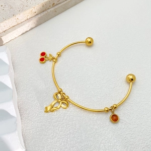 Detail of a gold open bangle featuring cherry charms and a polished bow decoration
