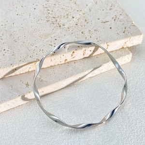 Elegant silver Mobius twist stainless steel bangle on a minimalist cream stone background