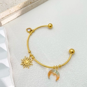 Close-up of golden open bangle with celestial sun, moon, and heart charms on stone base
